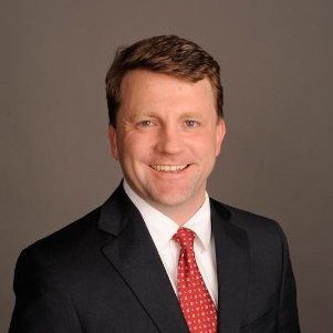 Headshot of a man with short reddish hair in a suit and red tie