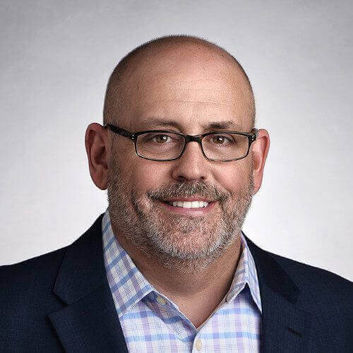 Headshot of a bald man with glasses and a goatee in a checked shirt